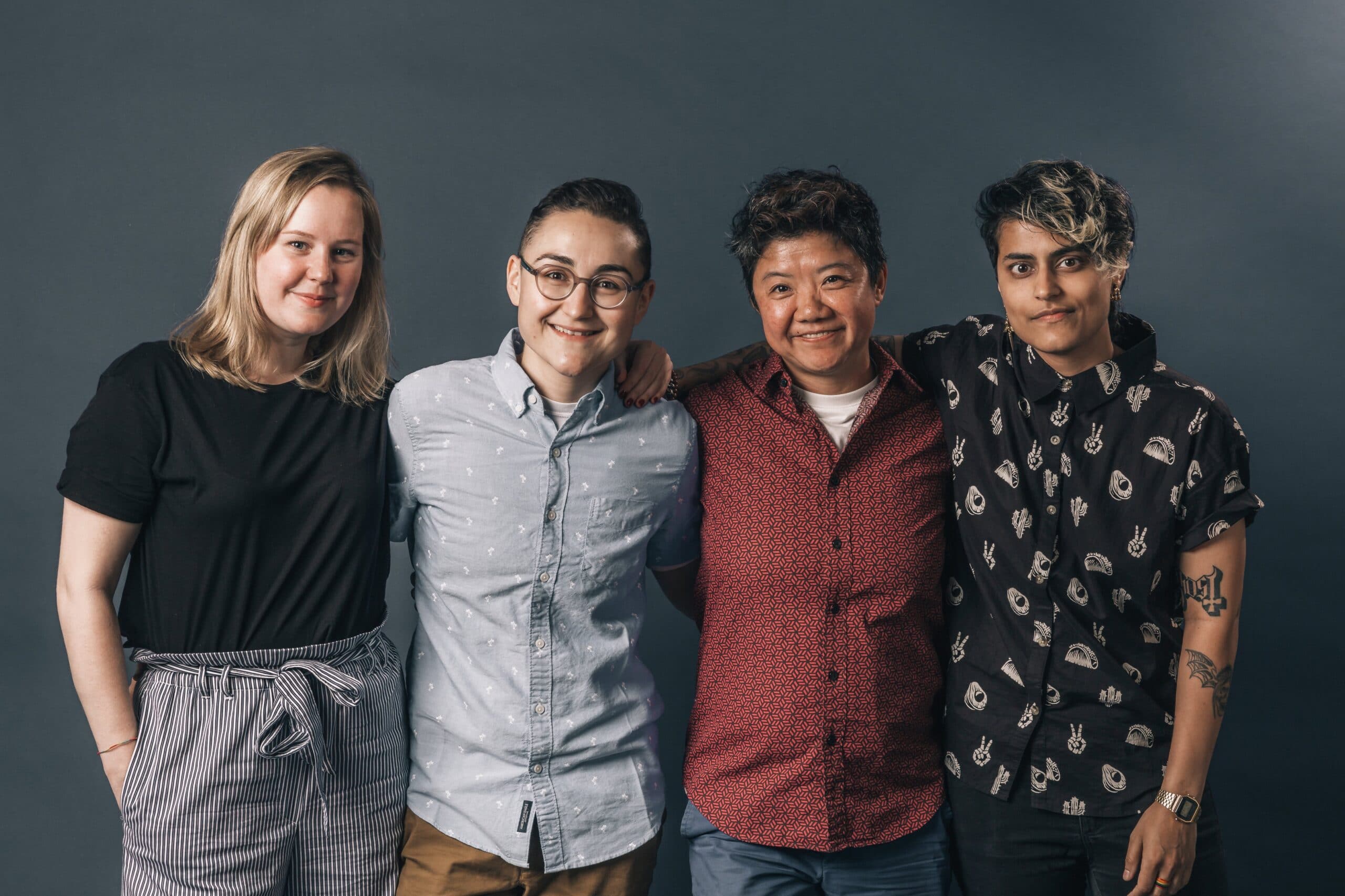 Four coworkers standing next to each other, smiling with their arms around each other.