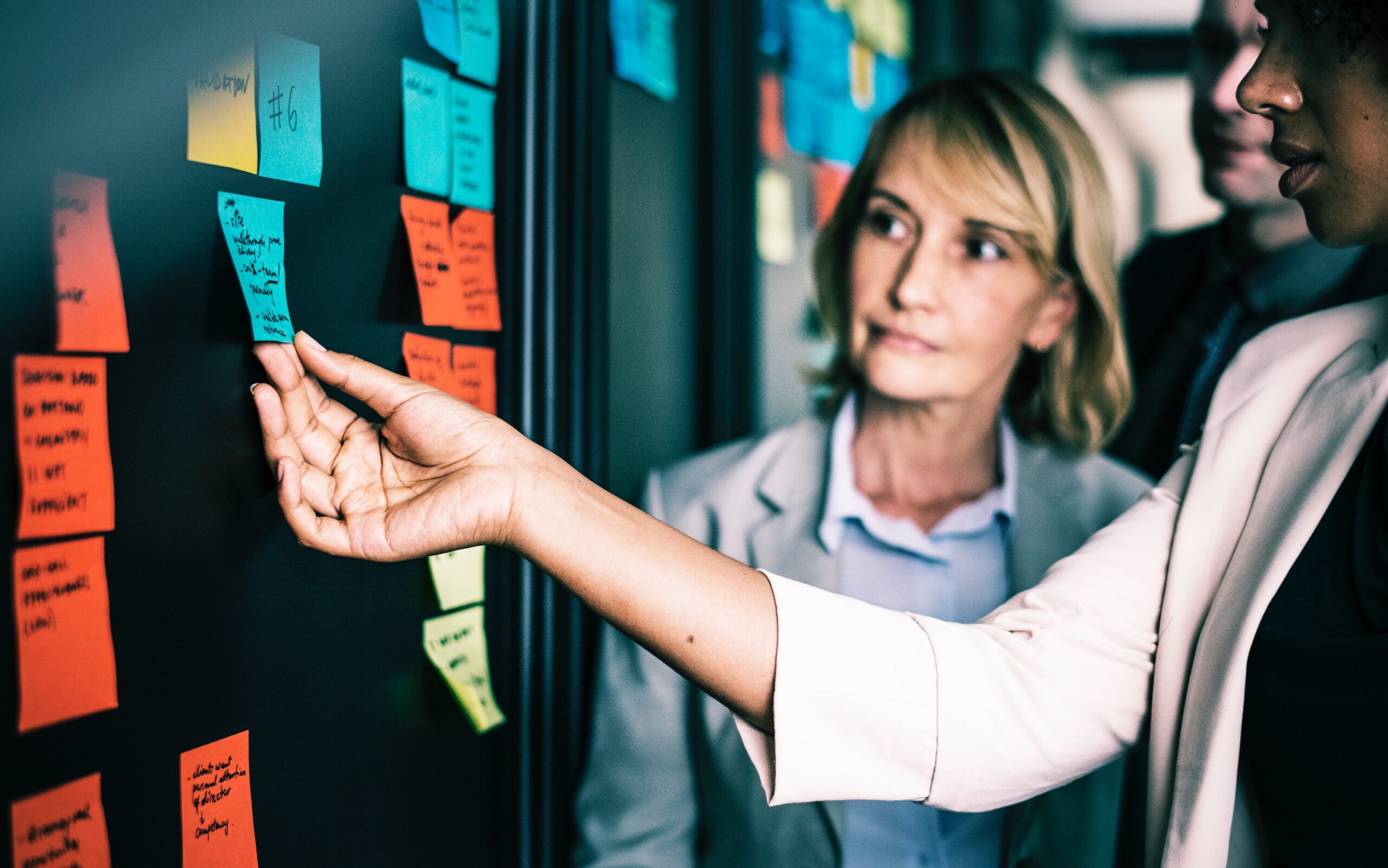 Two women delegating tasks on post it notes on an ideas board in an office space.