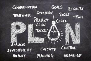 PLAN written on a blackboard with communication, teamwork, strategy, goals, planning, development, problems written around it